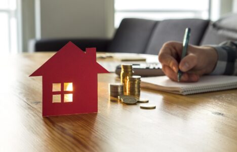 Property investor doing calculations on paper in front of model house and coins