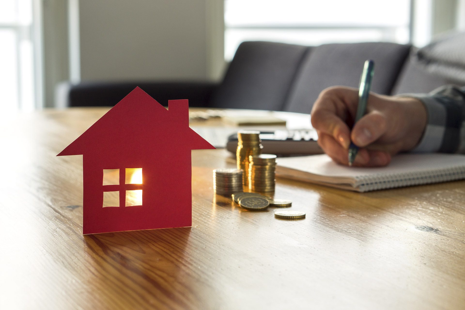 Property investor doing calculations on paper in front of model house and coins