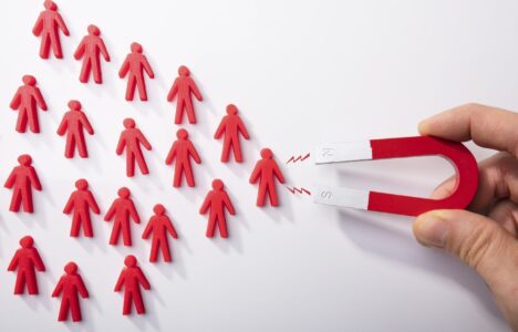 Close-up Of A Human Hand Attracting Red Human Figures With Horseshoe Magnet On White Background