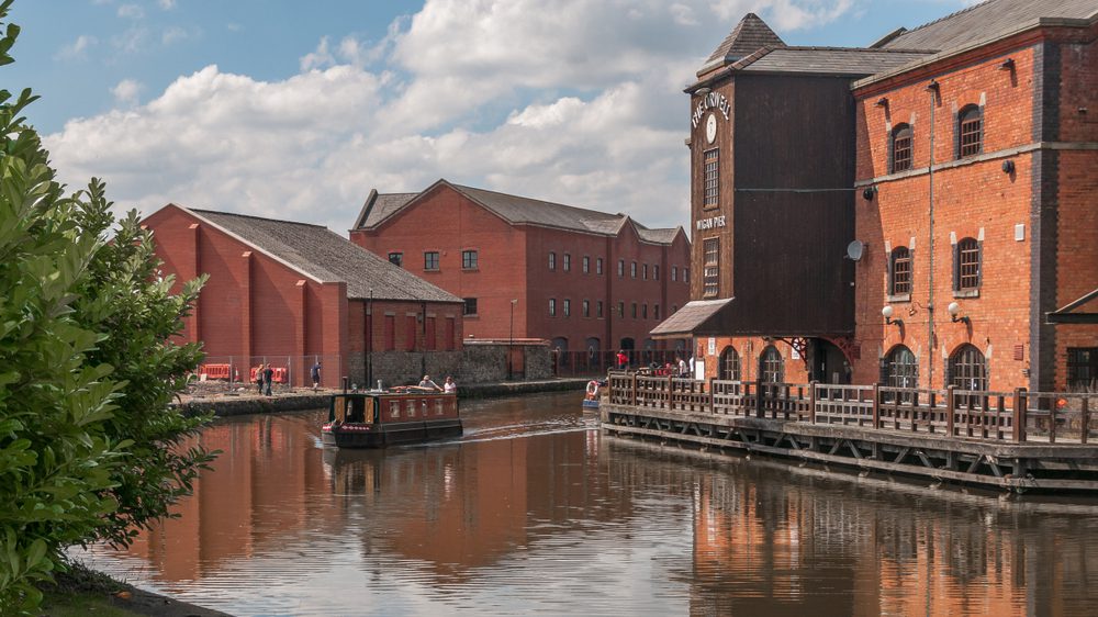 View of Wigan Canal with a canal boat passing by red brick buildings.