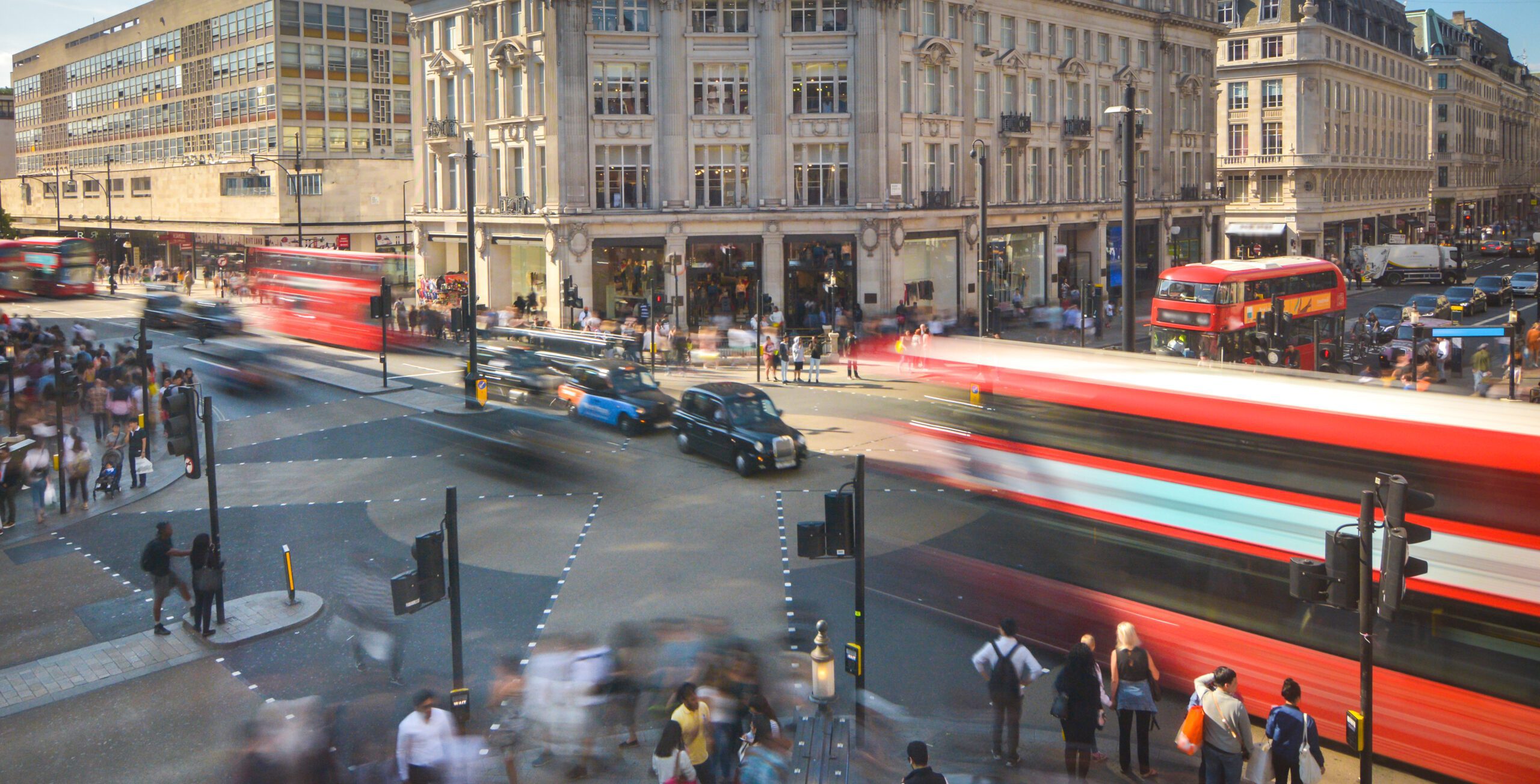 A high-level view of a busy London street, with various people and vehicles moving around. London properties stretch look over the street.
