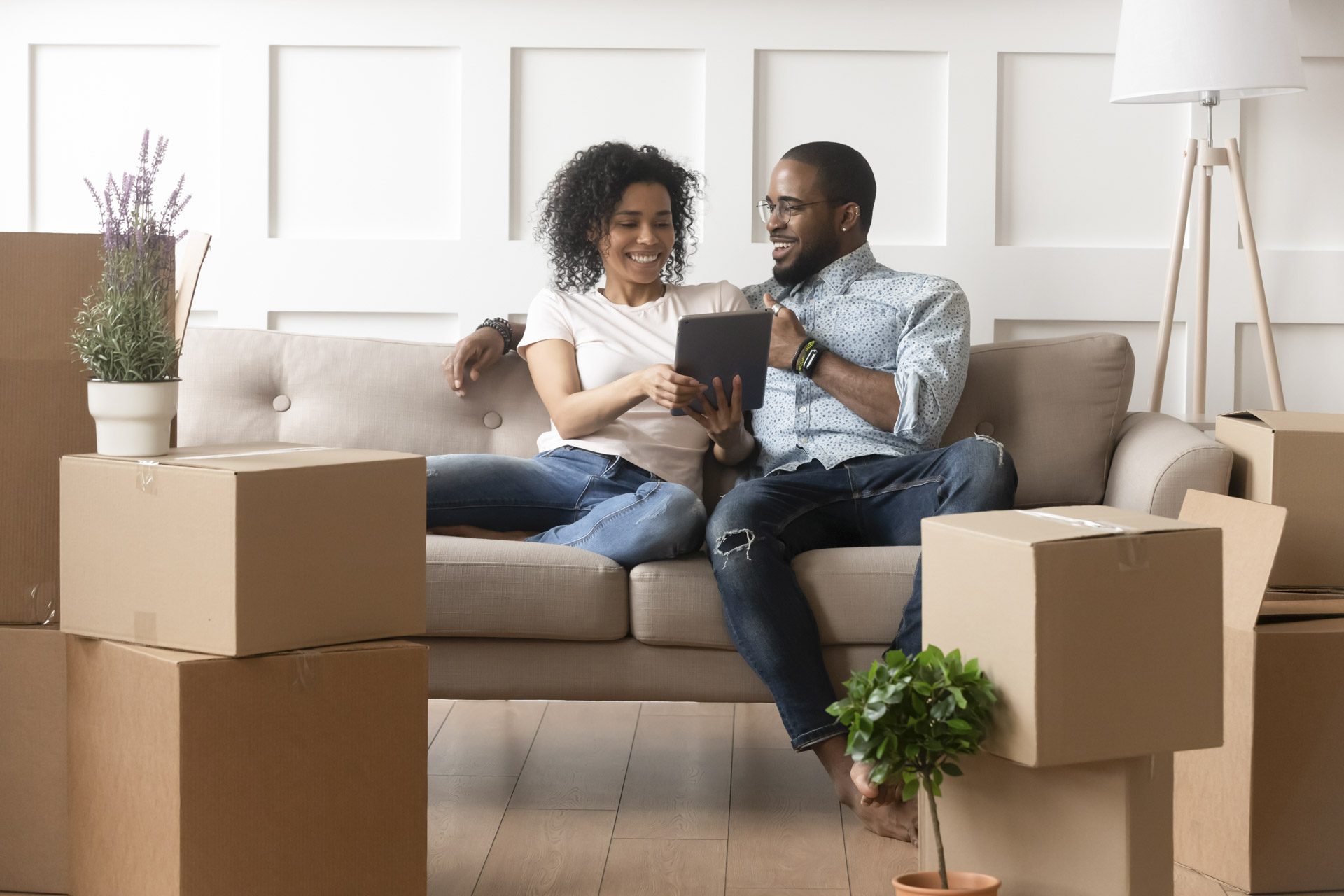 First-time buyers who have just moved into property sitting on couch and surrounded by moving boxes and household items