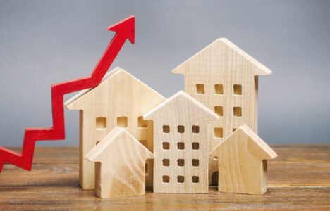 Miniature wooden houses with upward red arrow representing growing property prices and demand in rental market