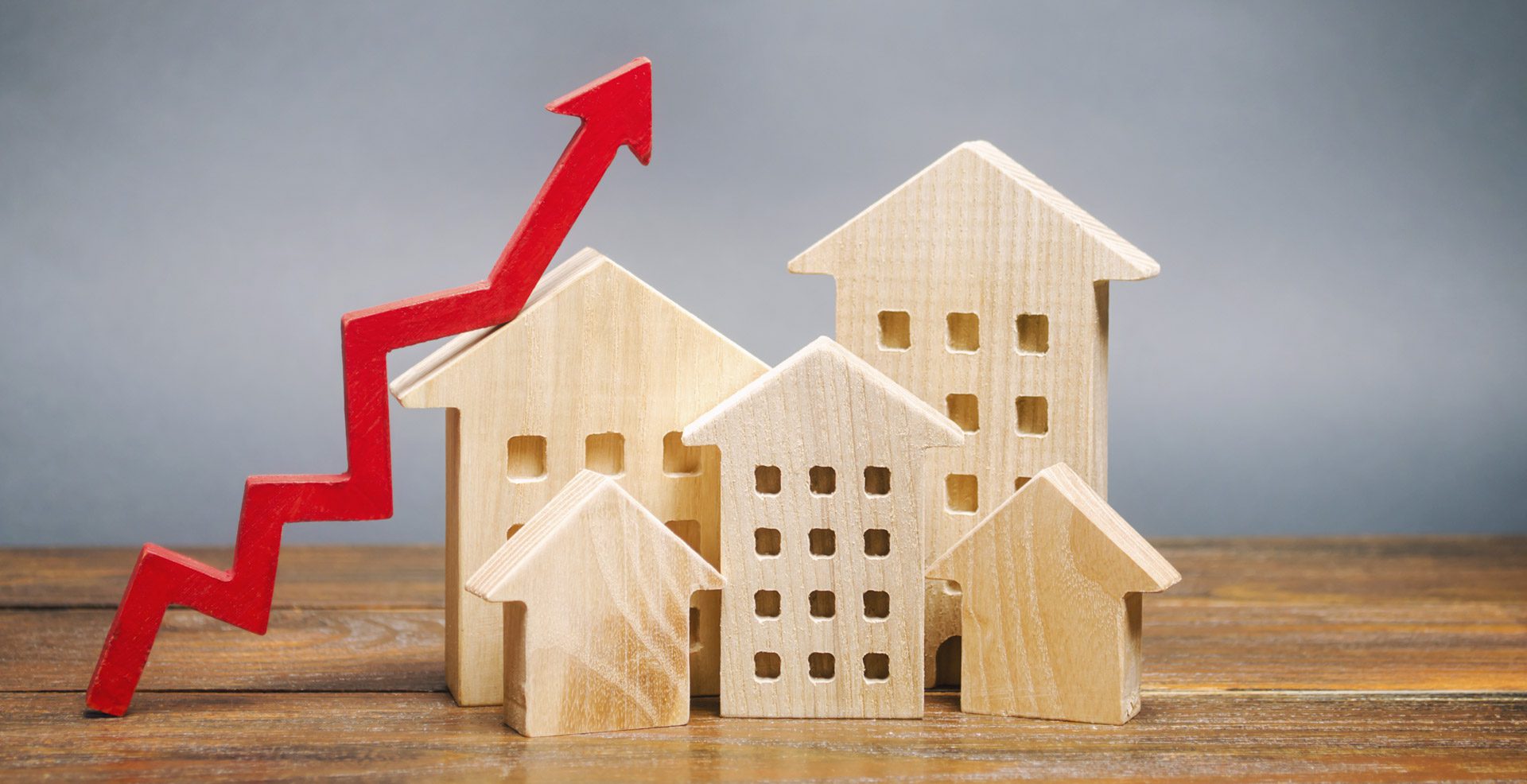 Miniature wooden houses with upward red arrow representing growing property prices and demand in rental market