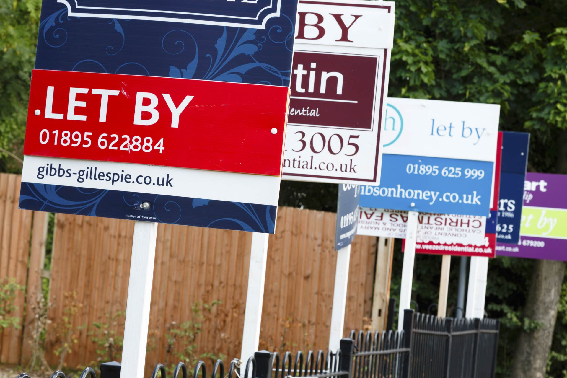 Estate agent "let by" signs line the road in a suburb of London representing a busy and active UK property market