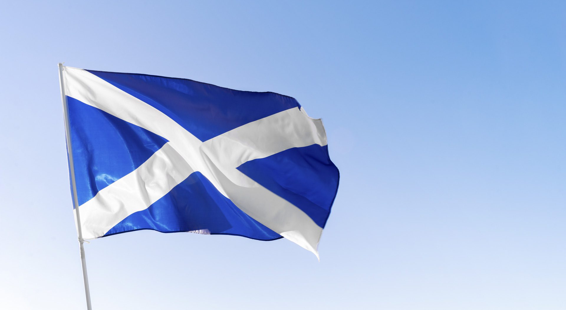 Flag of Scotland waving against blue sky
