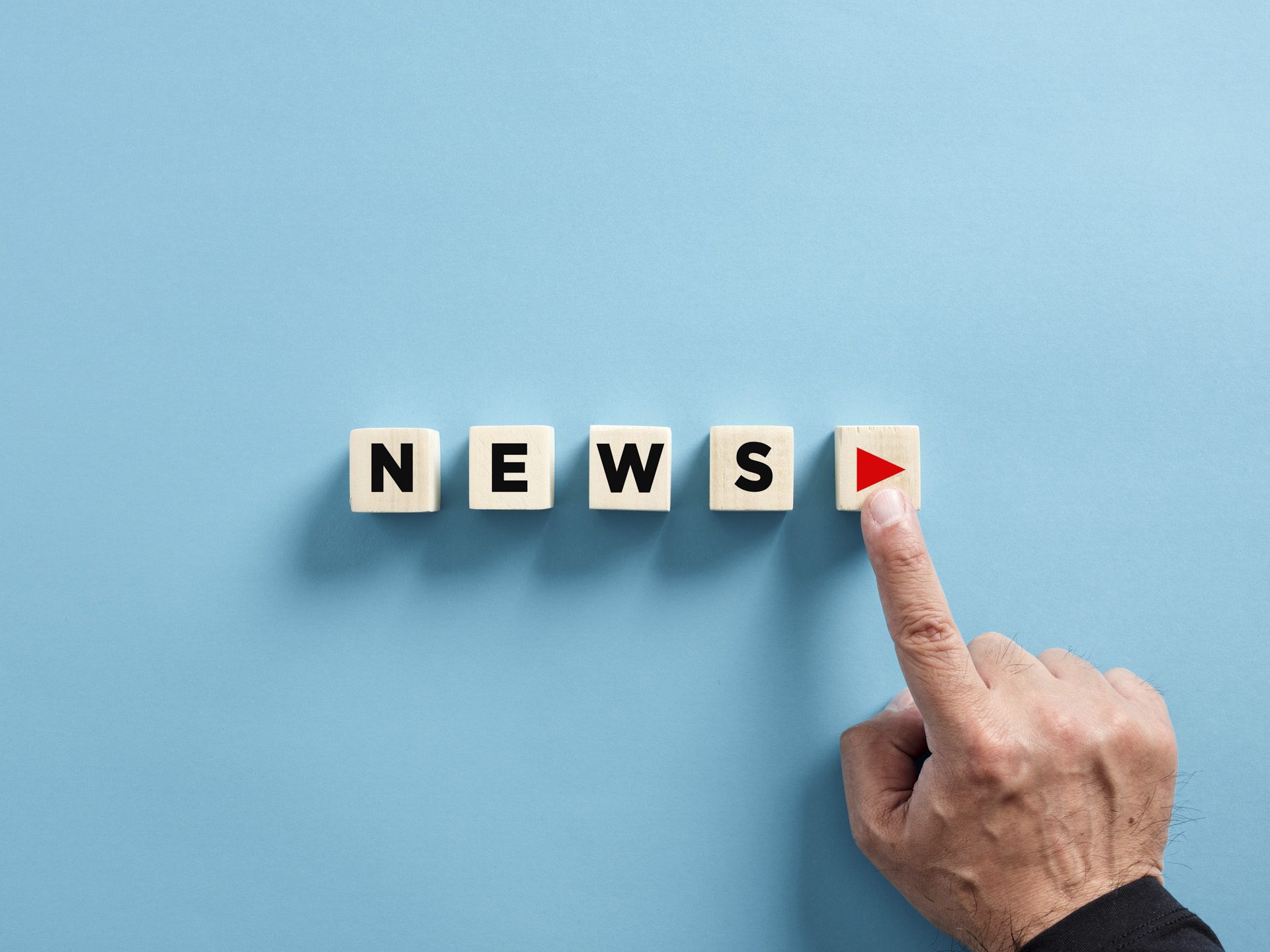 Male hand presses the play button with the news on wooden cubes. Broadcasting, publishing or watching the latest news concept.