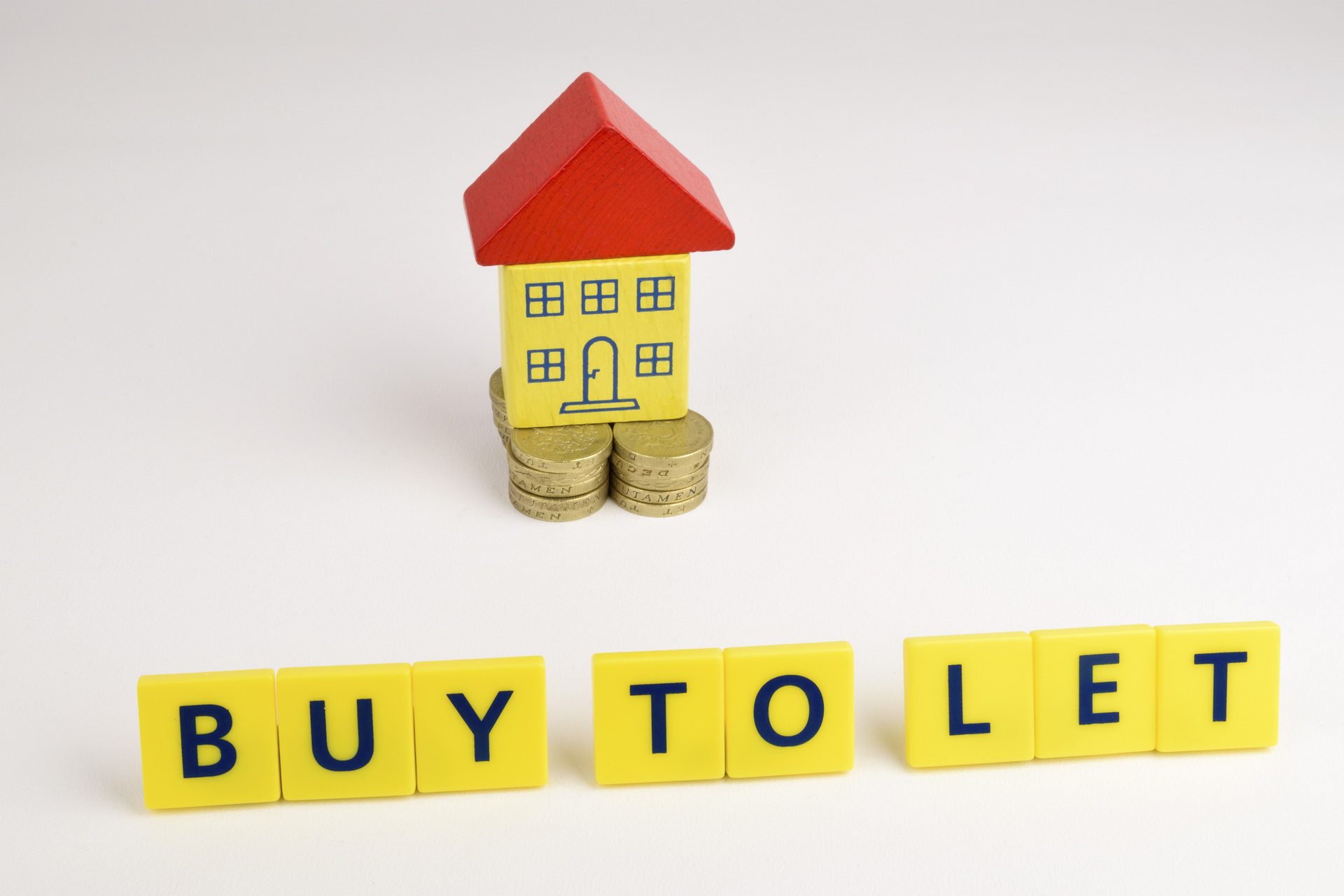 A toy house sitting on a stack of coins with the words 'Buy To Let' in front, representing property investment