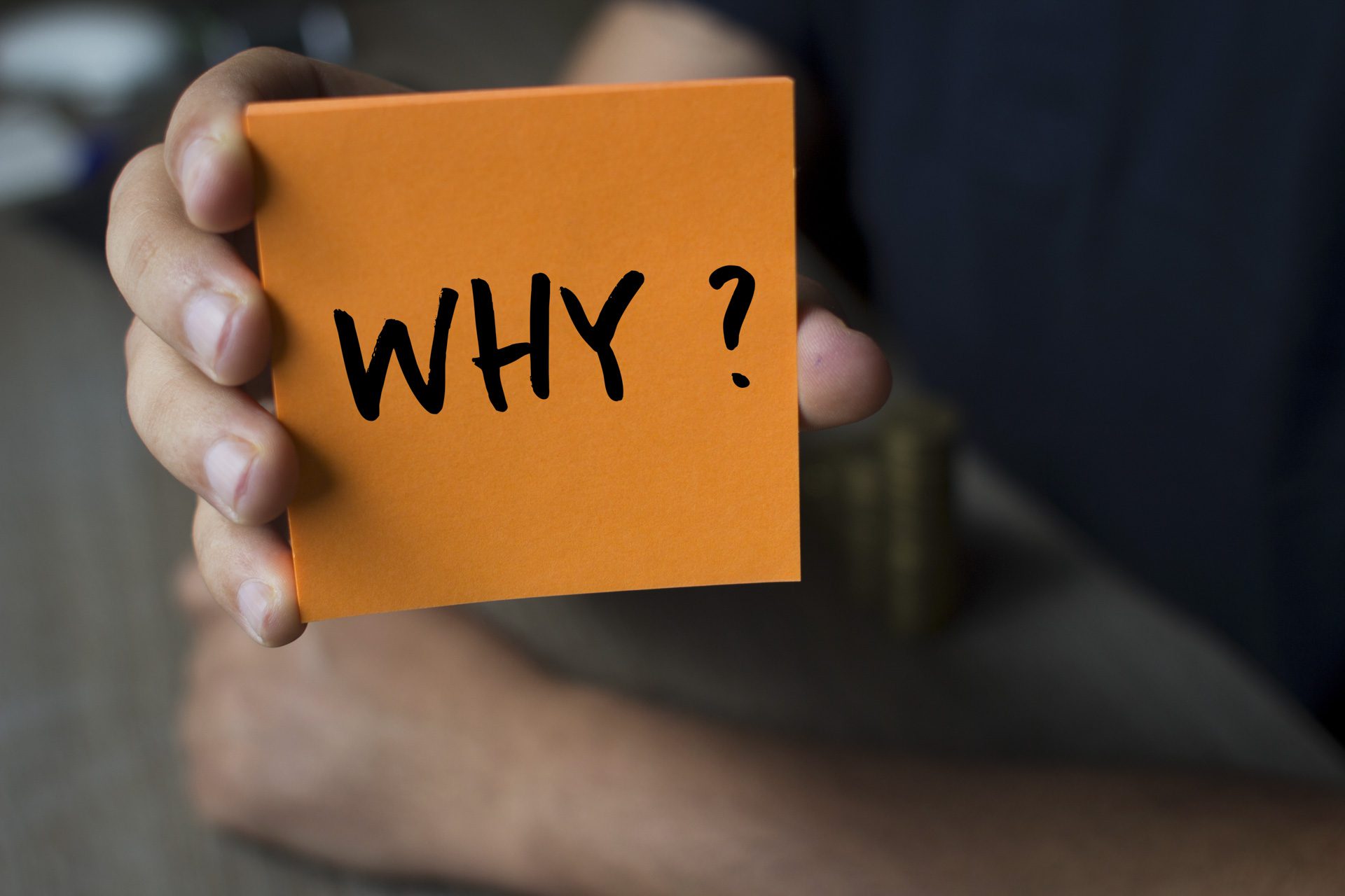 Hand holding an orange Paper with the word why - Why?, Business Concept