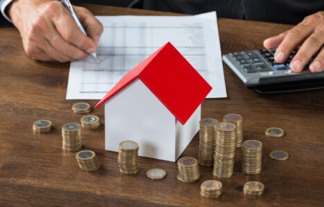Property investor makes calculations in front of wooden house and stacks of coins