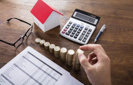 Property investor calculating tax with calculator, papers, coins and small house model