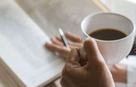 A person reading a book with a cup of coffee in their hand