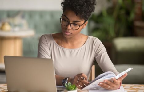 Lady flips book and looking at her laptop