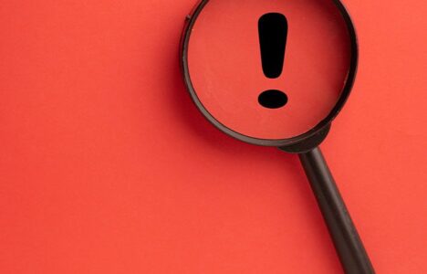 An exclamation mark inside a magnifier with red background