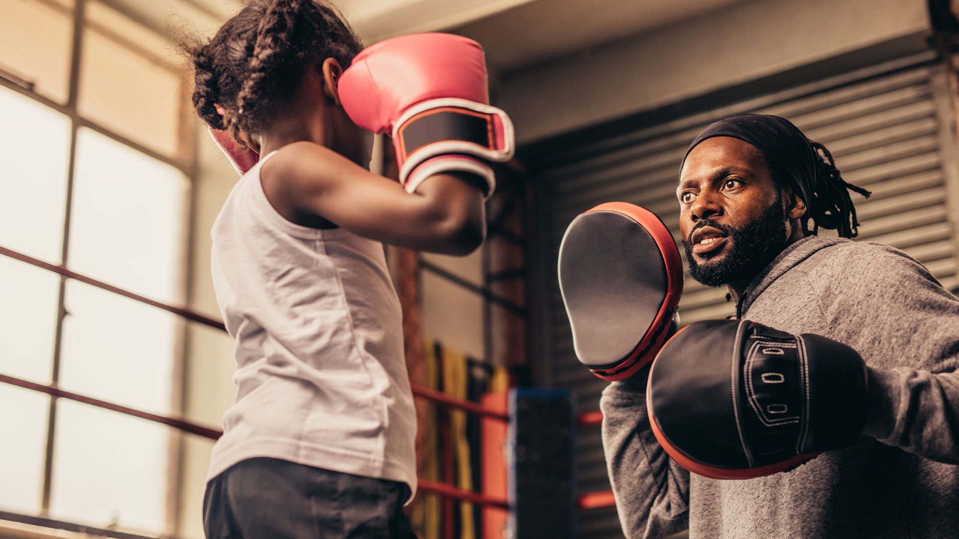 Adult and child doing boxing training with gloves in a gym