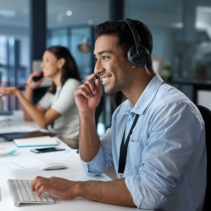 A man is speaking on the phone with a client at a computer with a headset representing customer service and communication