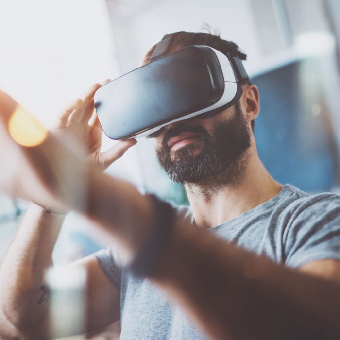 Closeup of bearded young man wearing virtual reality goggles in modern coworking studio.