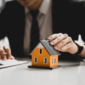 Man in a suit holding a mini model of a house