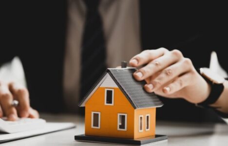 Man in a suit holding a mini model of a house