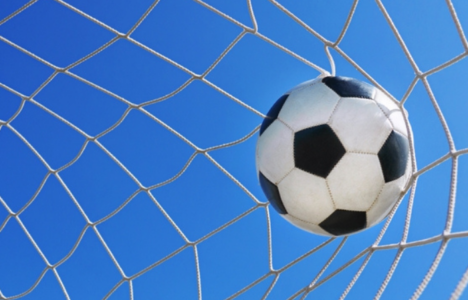 Football in goal net in a big stadium isolated on blue sky.