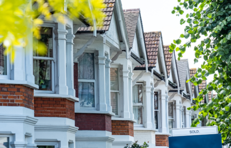 Row of terraced houses with 'sold' sign on a street with trees
