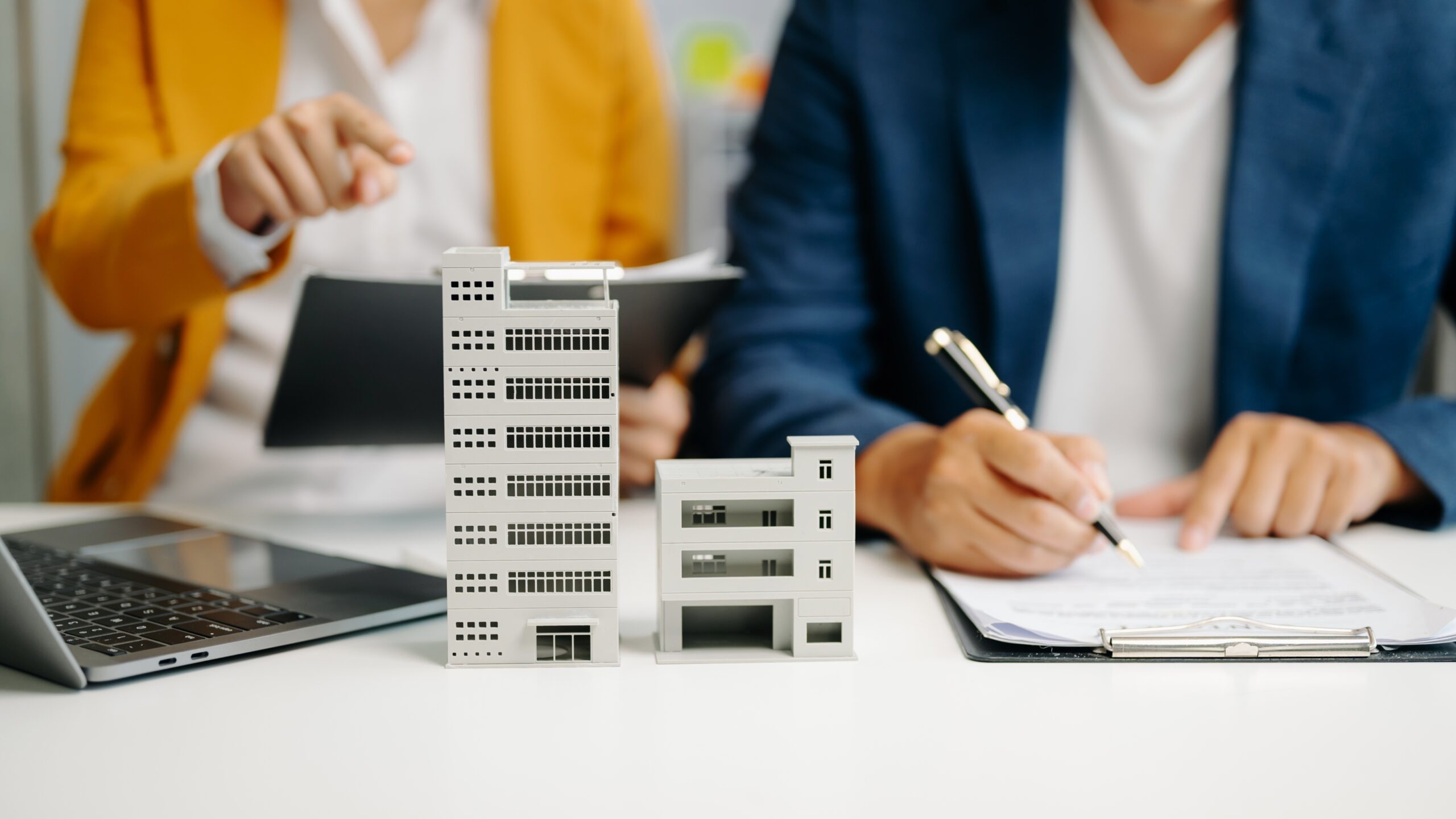 Two people conducting property investment business at a table with a model building and pen and paper
