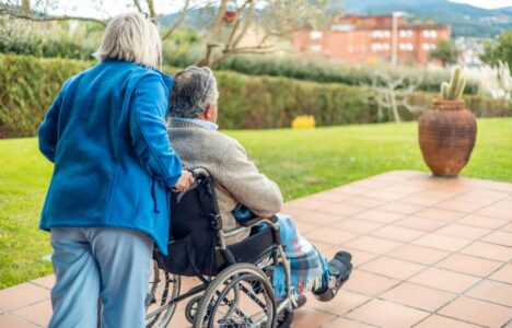 Nurse pushing elderly patient in wheelchair in garden of retirement home