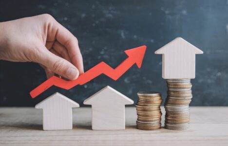 Hand holds red arrow pointing upwards beside house models