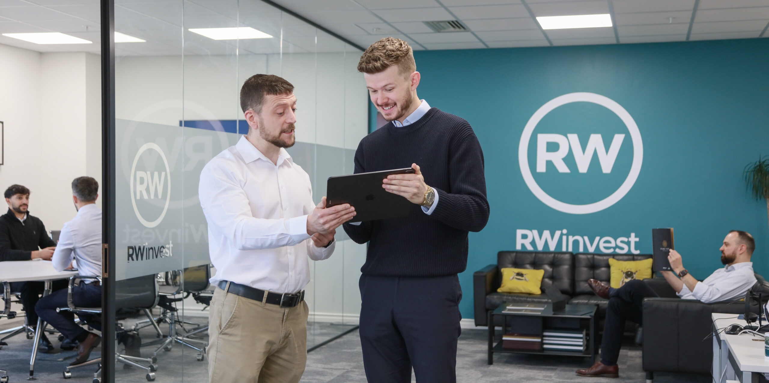 RWinvest Manchester office staff working next to wall with logo
