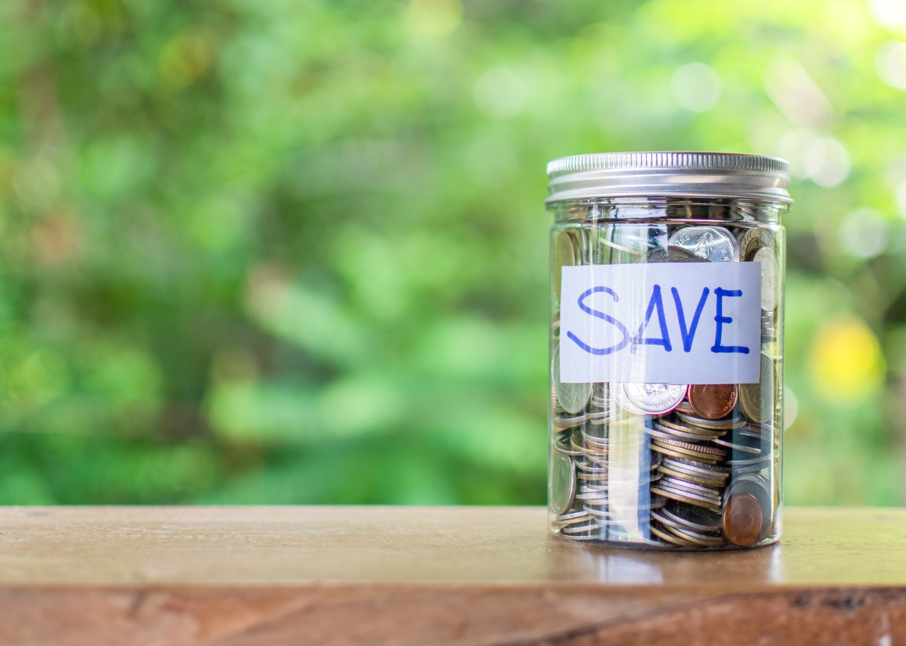 Coins and text SAVE in a glass jar placed on a wooden table