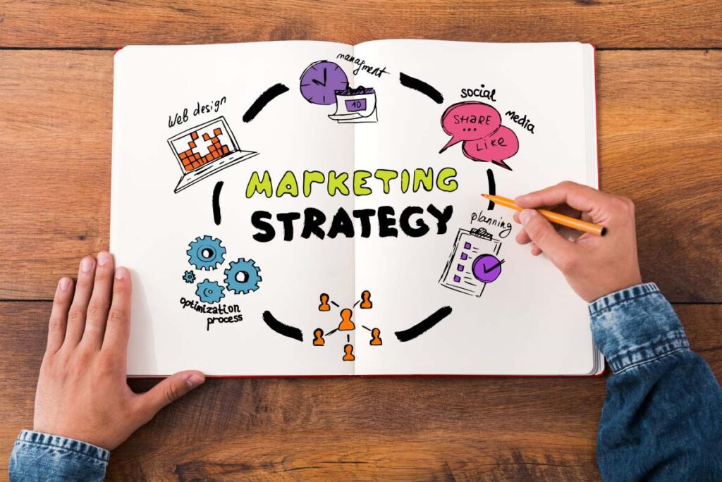person holding a pen and a paper with colorful sketches with the words marketing strategy written in the middle